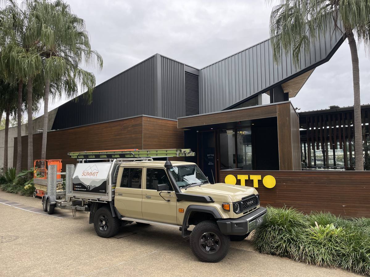 Summit Electrical ute and scissor lift parked outside a riverside restaurant